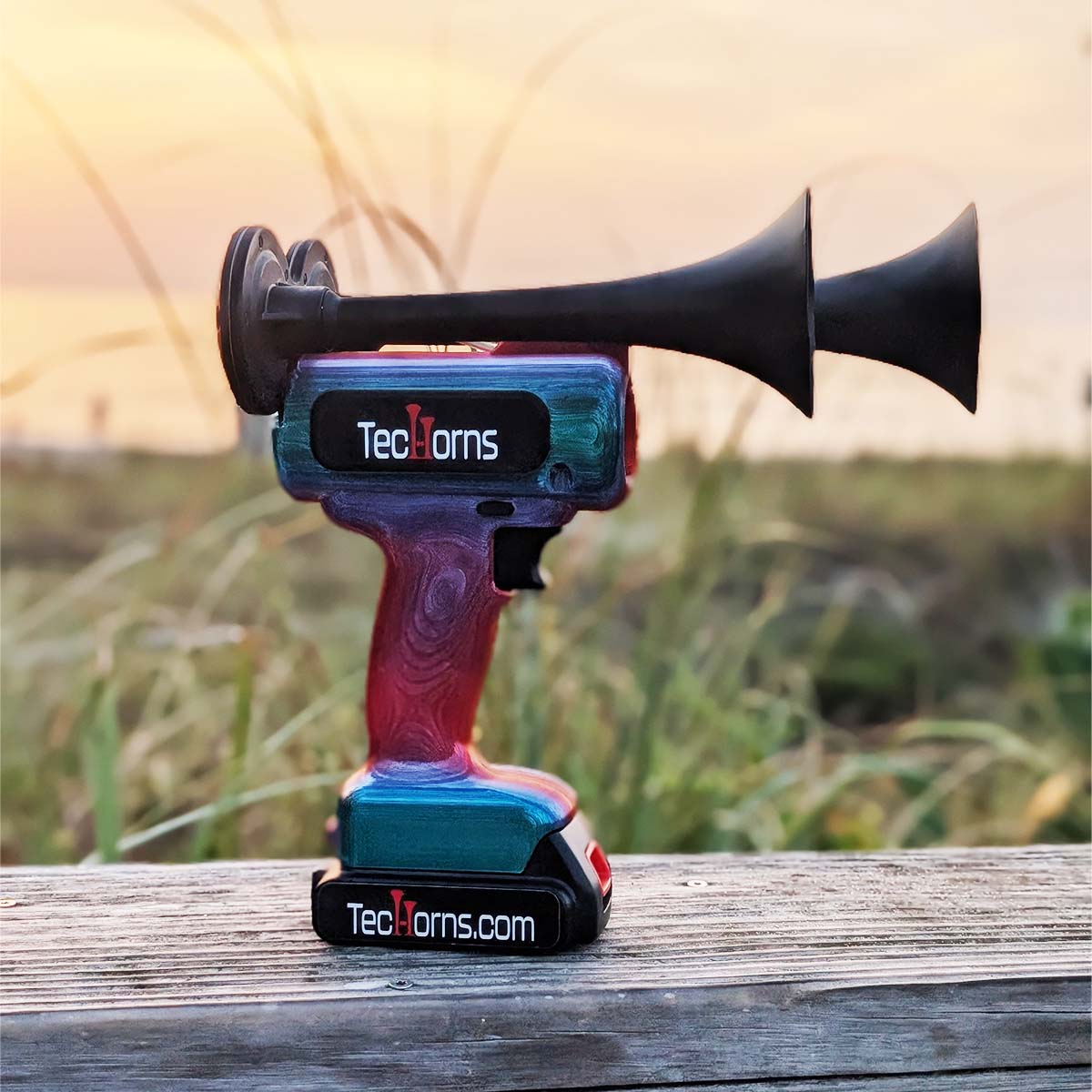 TecHorns Fire & Ice Candy 2-Horn – handheld train horn with 20 V lithium battery, featuring a red-to-blue candy finish captured at sunrise over the beach