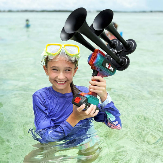 TecHorns Fire & Ice Candy 4-Horn – 130 dB handheld train horn with 20 V lithium battery, shown outdoors with a young girl holding the horn in shallow beach water
