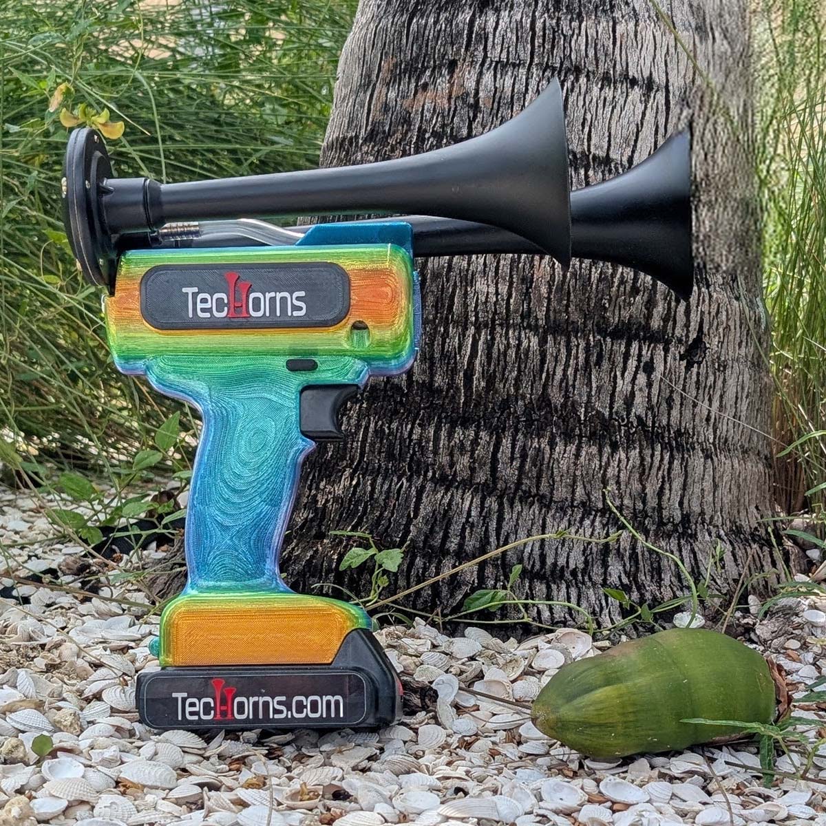 TecHorns Mango Bay Candy 2-Horn – 130 dB handheld train horn with 20 V lithium battery, shown outdoors with a tropical coconut tree in the background highlighting its bright mango-to-aqua candy fade