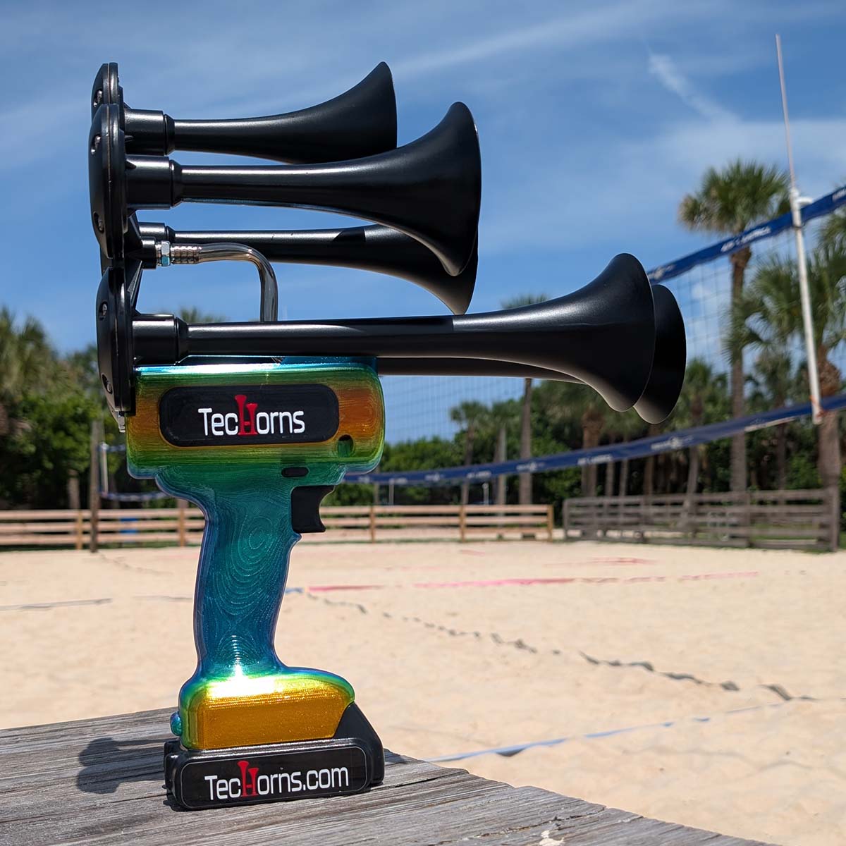 TecHorns Mango Bay Candy 5-Horn – handheld train horn with 20 V lithium battery, shown near a beach volleyball court with its vivid mango-to-aqua candy fade capturing the tropical summer vibe