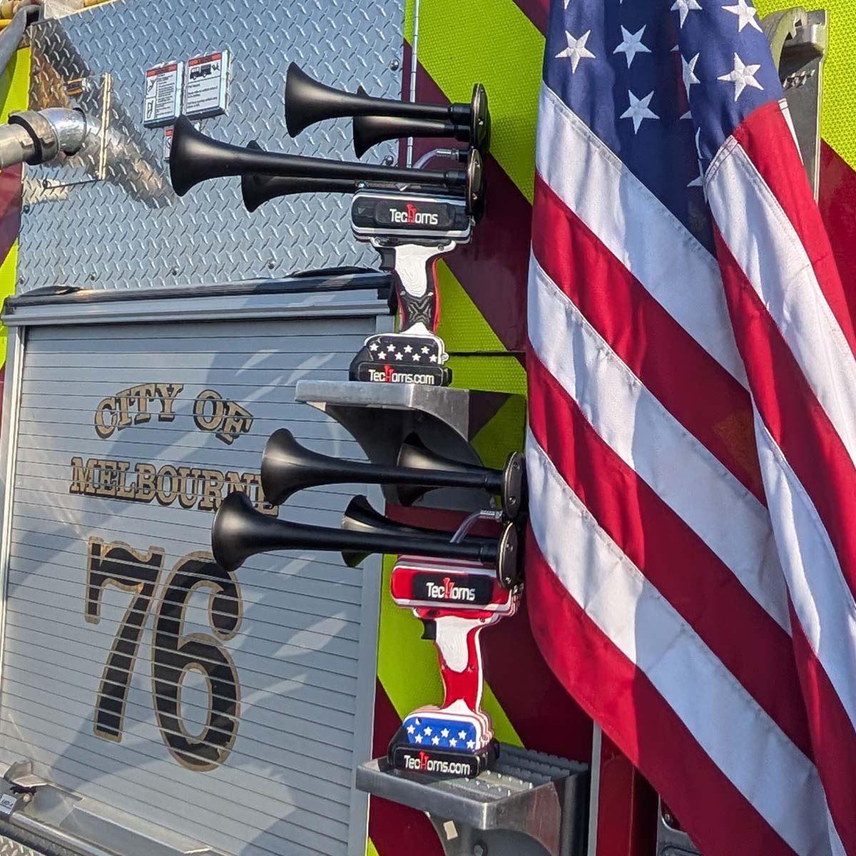 TecHorns ‘Merica 4-Horn – handheld train horn with 20 V lithium battery, shown beside Thin RED Line horns on the back of a fire truck next to an American flag, symbolizing pride and power