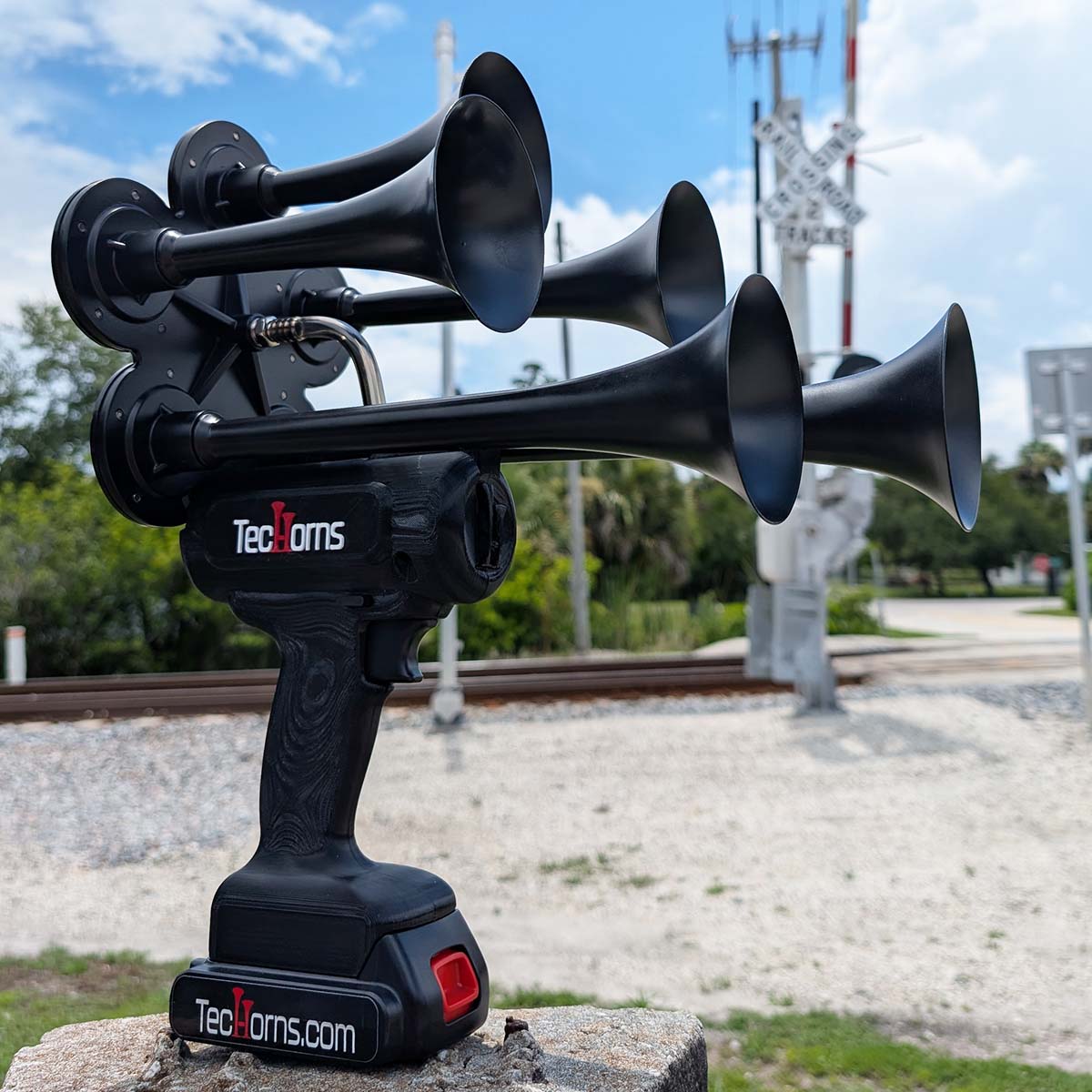 TecHorns Satin Black 5-Horn – 130 dB deep-tone handheld train horn with 20V lithium battery and charger, photographed in front of a railroad crossing