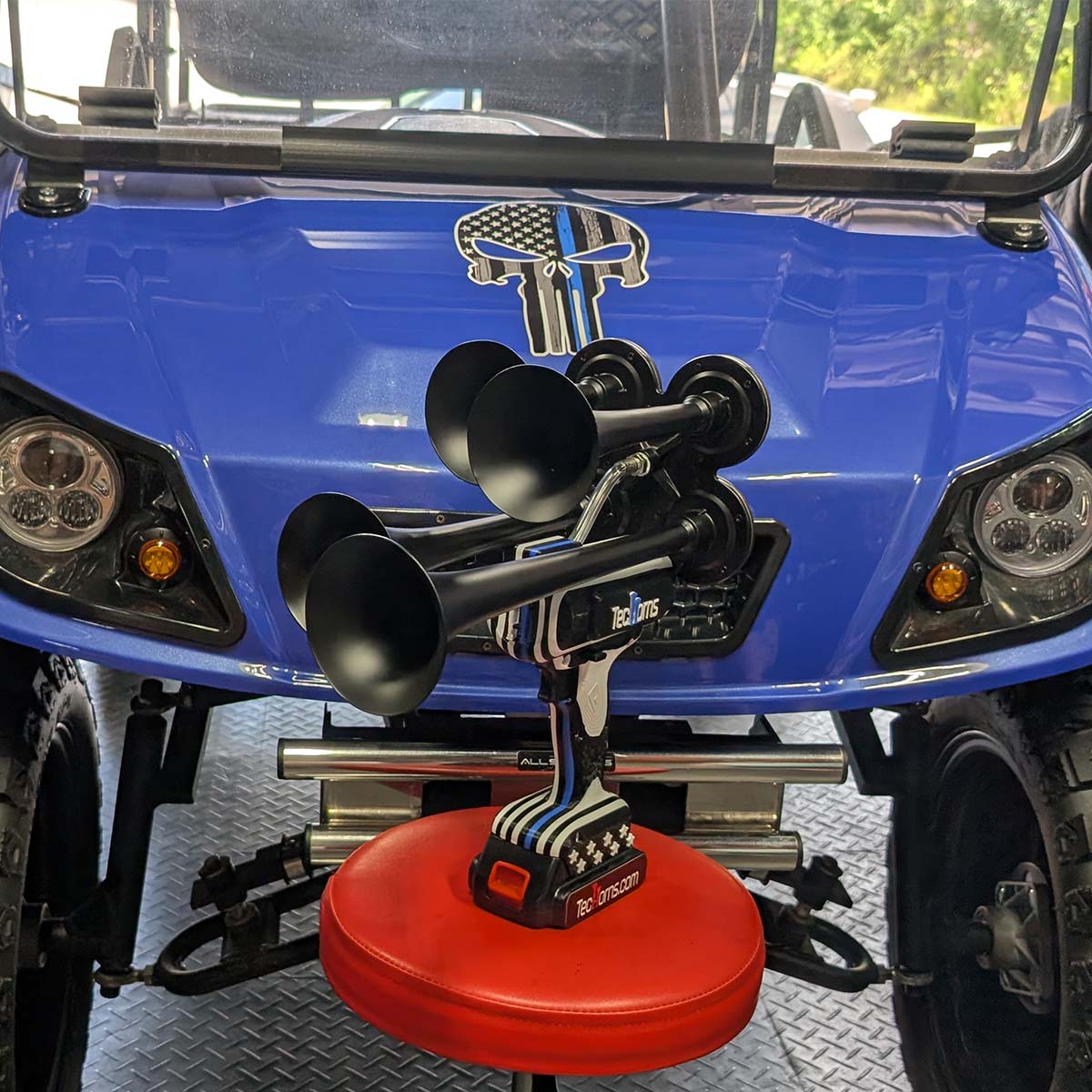 Thin BLUE Line TecHorns 4-Horn – handheld train horn with 20 V lithium battery, displayed on a mechanic’s stool in front of a custom blue golf cart with a Thin BLUE Line Punisher decal