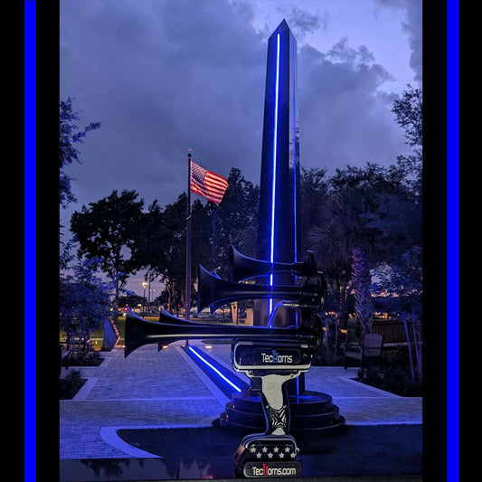 Thin BLUE Line TecHorns 5-Horn – handheld train horn with 20 V lithium battery, photographed at a fallen officer memorial with the American flag in the background, symbolizing honor, unity, and sacrifice