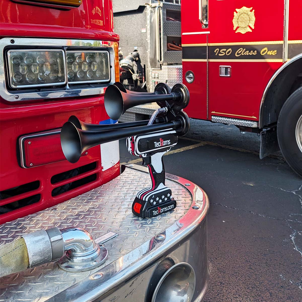 Thin RED Line TecHorns 4-Horn – handheld train horn with 20 V lithium battery, displayed on the front bumper of a fire truck with red body and department emblem visible, honoring firefighter courage and unity