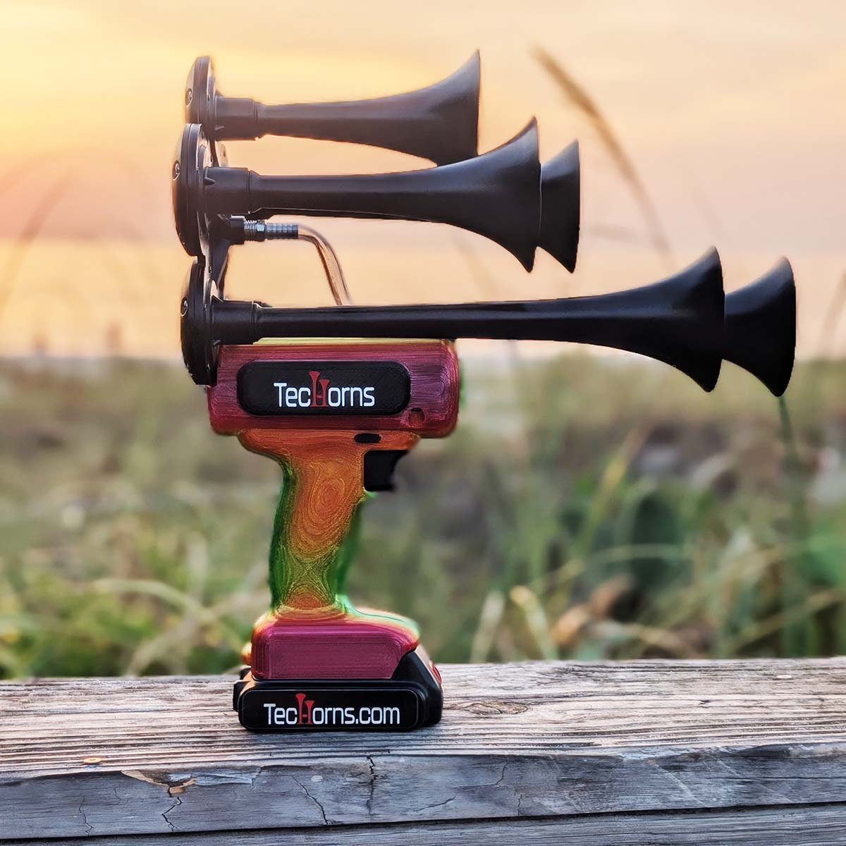 TecHorns Tropical Blaze Candy 5-Horn – handheld train horn with 20 V lithium battery, showcasing the red-orange-green candy fade finish at sunrise by the beach