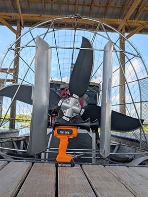Orange TecHorn 2-Horn handheld train horn with 20 V lithium battery displayed in front of an airboat propeller, highlighting Florida-inspired design and outdoor adventure use