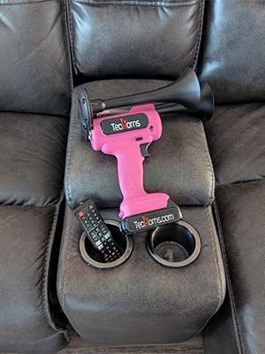 TecHorn Pink 2-Horn – compact handheld train horn with 20 V lithium battery and black trumpets, displayed on a couch highlighting its playful color and modern design