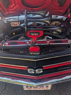 Red and black TecHorn 5-Horn handheld train horn with 20 V lithium battery displayed under the hood of a classic 1970 Chevelle SS, combining modern power with vintage muscle car style