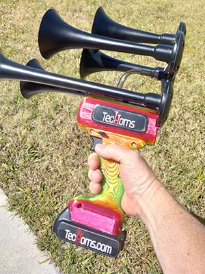 TecHorn Tropical Blaze 5-Horn – handheld train horn with 20 V lithium battery and vibrant candy-fade finish blending red, orange, and green, shown in hand for a detailed close-up view
