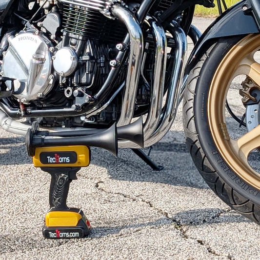 TecHorns Black and Gold 2-Horn – dual color handheld train horn, 130 dB with 20V lithium battery, photographed in front of chrome motorcycle exhaust pipes