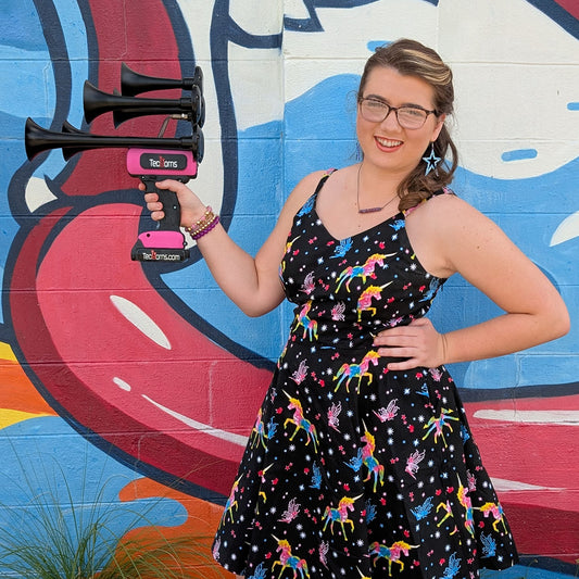 TecHorns Black and Pink 5-Horn – dual color handheld train horn, 130 dB with 20 V lithium battery, held by young woman in black and bright dress standing before colorful graffiti mural