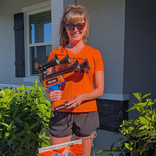 TecHorns Blue and Orange 4-Horn – dual color handheld train horn, 130 dB with 20V lithium battery, held by woman wearing University of Florida Gators shirt