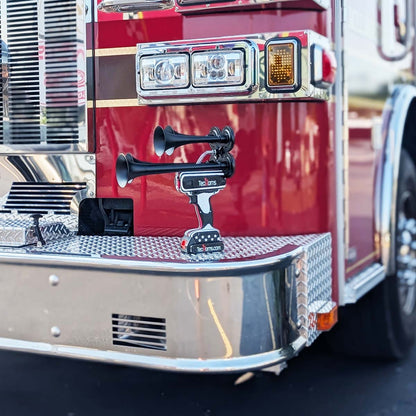 Thin RED Line TecHorns 4-Horn – handheld train horn with 20 V lithium battery, displayed on the chrome front bumper of a fire truck with red paint and gold striping, honoring firefighters and the Thin RED Line of courage